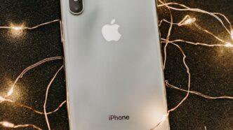 A sleek smartphone lies on a glittering black surface adorned with warm string lights, showcasing modern technology.