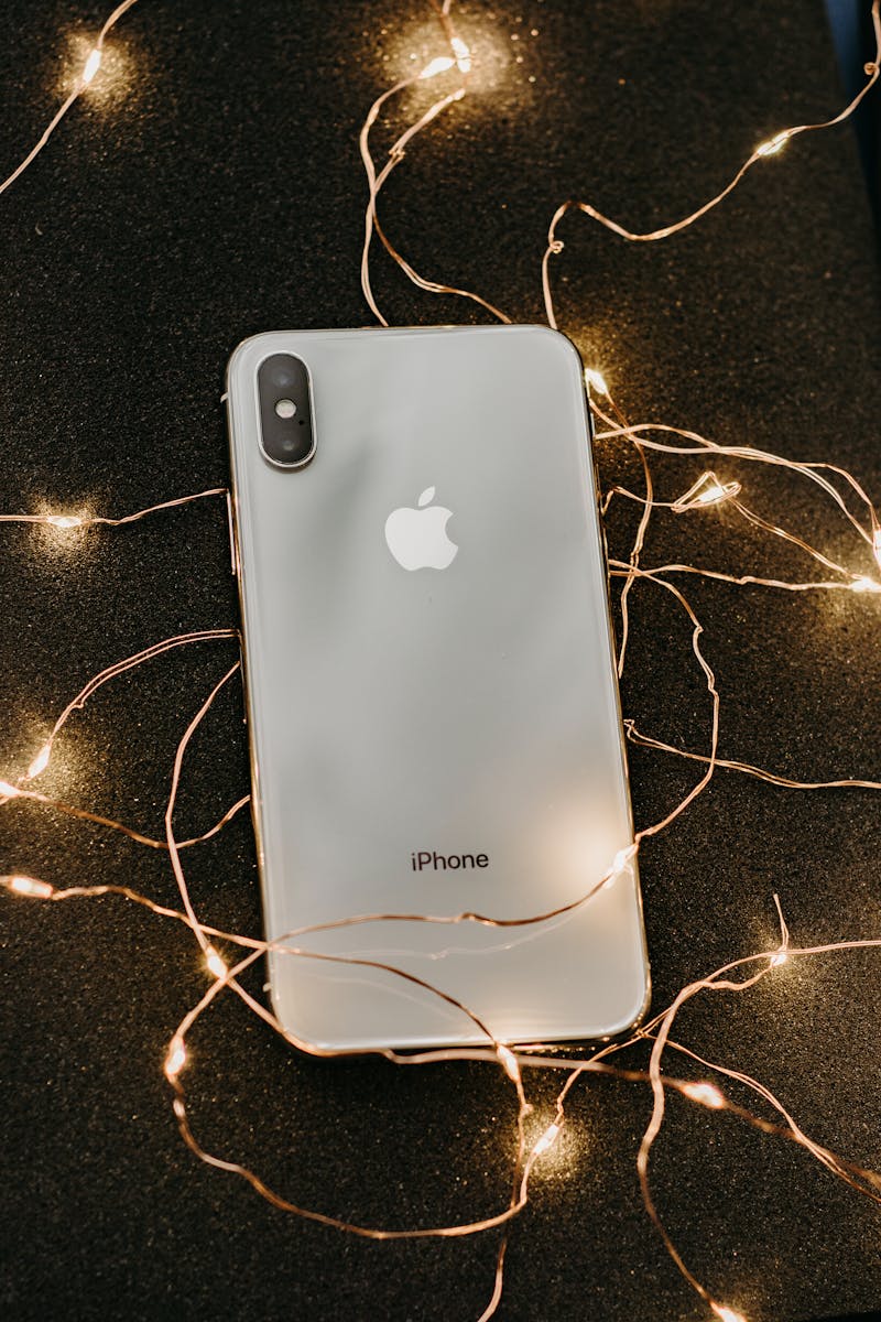 A sleek smartphone lies on a glittering black surface adorned with warm string lights, showcasing modern technology.