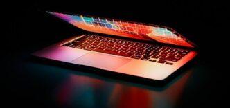 Laptop partially opened, emitting vibrant multicolored lights in dark setting.