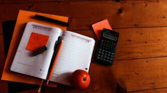 black scientific calculator, orange, and notebook on table