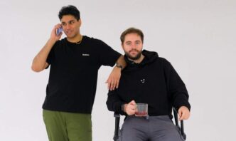 a man sitting in a chair next to another man on a cell phone
