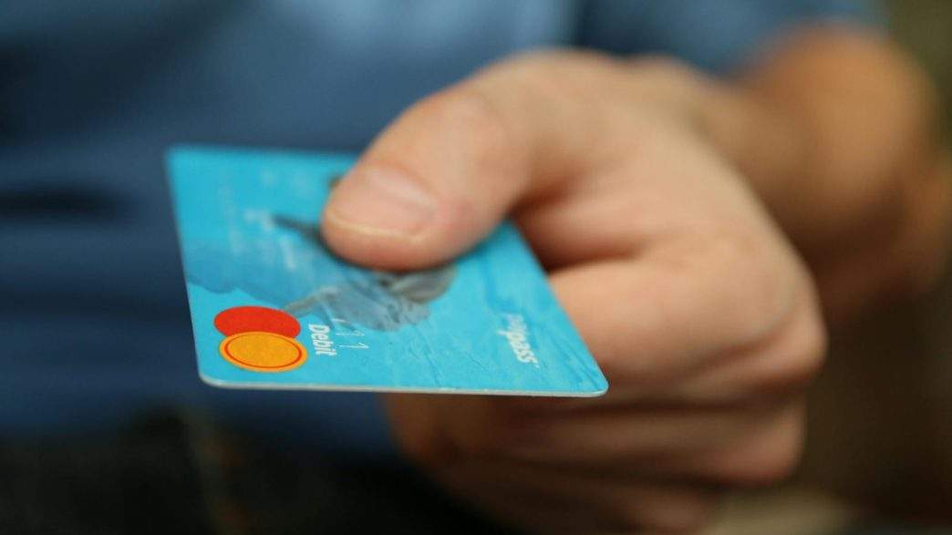 27 Best Stripe Alternatives To Accept Payments In Your Business 1 A close-up shot of a hand offering a blue debit card for payment.