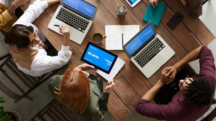 Diverse team discussing business strategies with laptops and tablets at a wooden table.