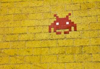 55 Reasons Why Fighting Bitcoin Spam Won't Work 8 Street art featuring a retro pixelated space invader on a vivid yellow brick wall.