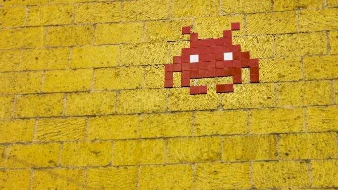 Street art featuring a retro pixelated space invader on a vivid yellow brick wall.