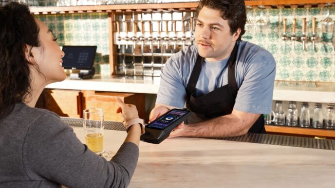 Customer using smartwatch for contactless payment at the bar with a handheld POS system.